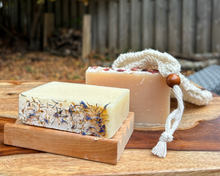 Bar of lavender soap on a wooden soap dish and a rose soap and soap saver bag on a table in nature