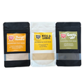 Three stand-up pouches of Mood Indigo face masks powders arranged side by side on a white background: Mango Mamma Nourishing Face Mask, Rise & Shine Refreshing Face Mask, and Exotic Aft Cleansing Face Mask.