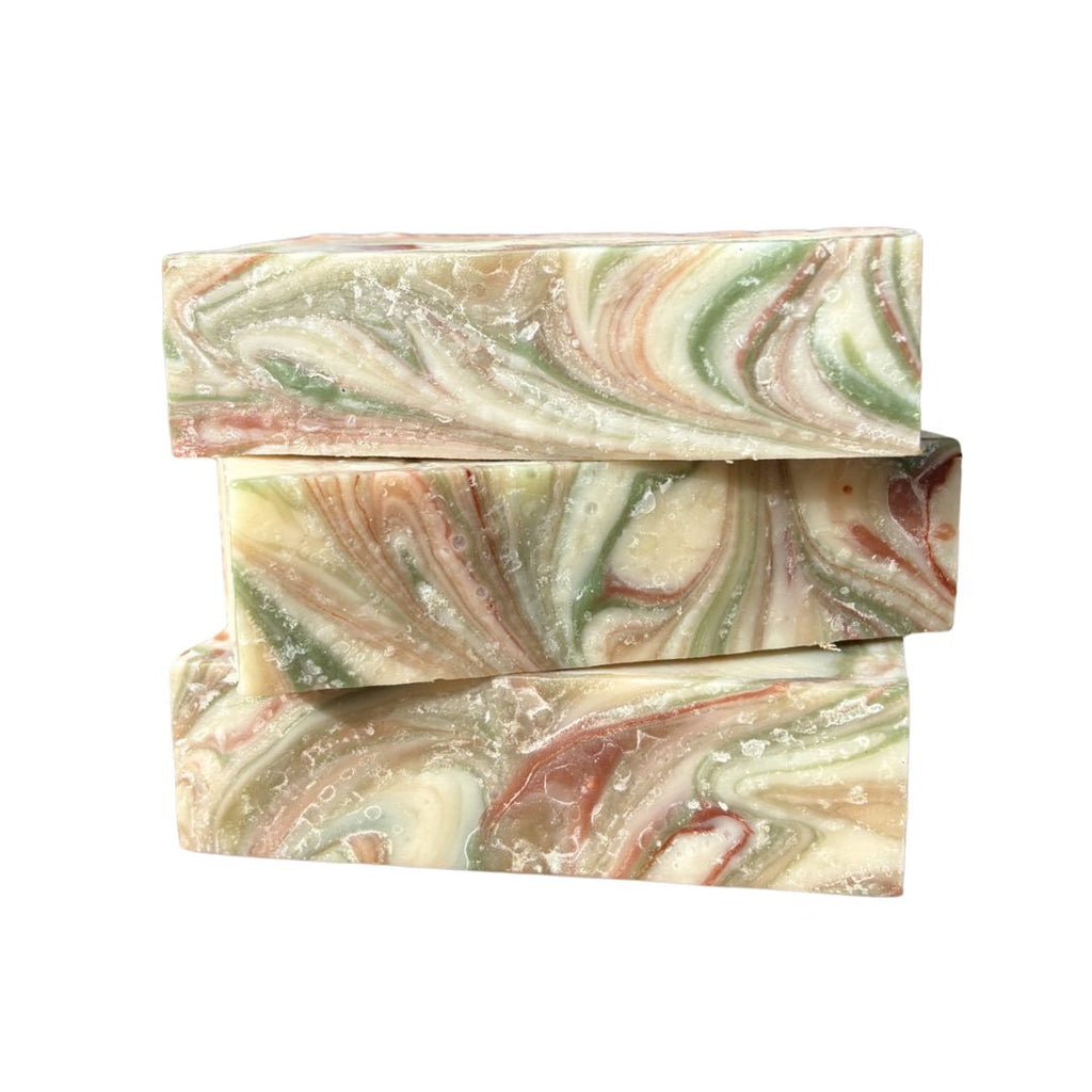 Three swirled grapefruit essential oil soap bars in green, pink, and beige on a white background