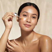Woman applying a Mood indigo face oil with a dropper of Exotic-ah day face oil to her face against a beige backgr