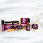 A curated wellness Patchouli gift set featuring Happy Hippie brand products, including body butter, body oil, a soap bar, a packaged bath bomb, a wooden spatula, and a small roll on perfume bottle, arranged on a white fabric background. Made by Mood indigo as part of their Earthy and Grounding collection, Happy Hippie