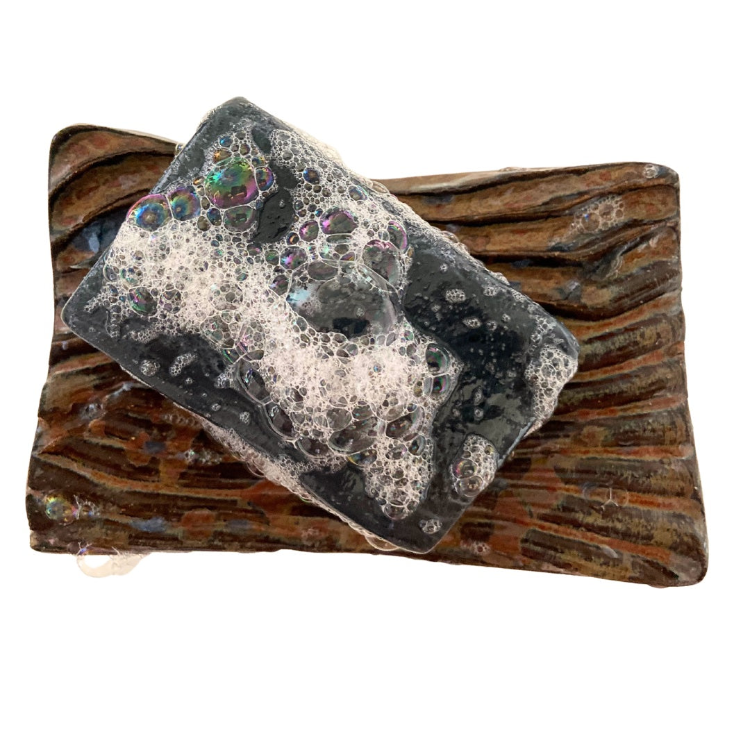 Limited edition activated charcoal and tulsi black bar soap lathering on a handmade ceramic soap dish, crafted by Mood Indigo Living in North Carolina