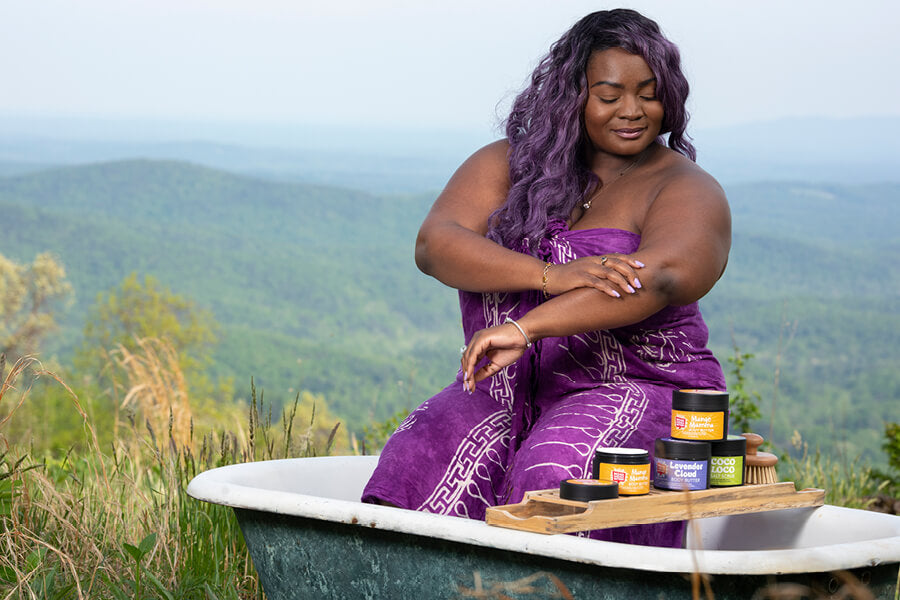 Woman sitting on the edge of a tub putting on body butter.
