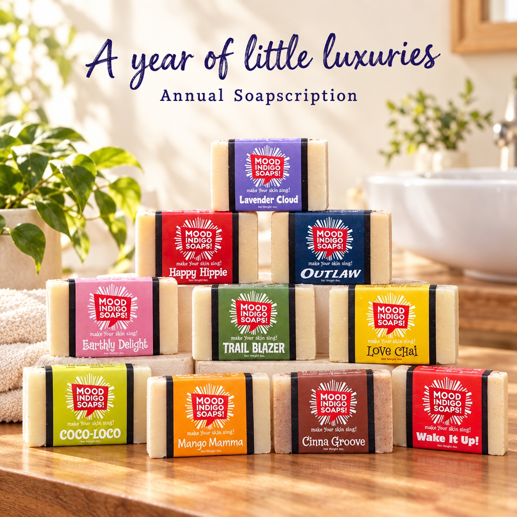 Ten Mood Indigo soap bars in colorful packaging stacked on a sunlit bathroom counter beneath “A year of little luxuries” and “Annual Soapscription.”