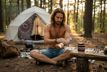 Young man applying Patchouli Body Butter outdoors at camping site - natural bohemian skincare for outdoor enthusiasts